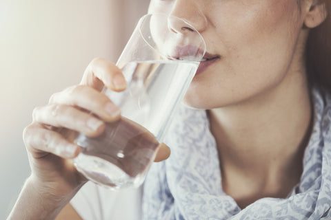 A woman drinking a glass of water, possibly after taking a L-Lysine supplement to support her immune system.